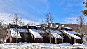 A log cabin with a steeply pitched roof, surrounded by snow-covered ground and trees. - Ski Access from this Kettlebrook Condo with Modern Kitchen (Ludlow)