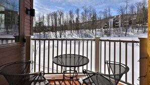 A covered outdoor area with a table and chairs, a white railing, and a view of a snowy landscape with trees and buildings. - Ski Access from this Kettlebrook Condo with Modern Kitchen (Ludlow)