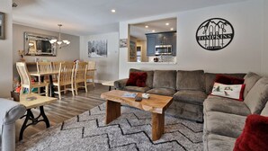 A modern living room with a wooden dining table, grey sofa, and a coffee table. - Ski Access from this Kettlebrook Condo with Modern Kitchen (Ludlow)