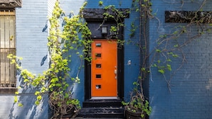 Un edificio azul con una puerta naranja y plantas en macetas.