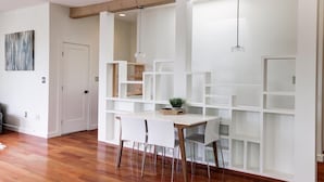Un comedor moderno con una mesa y sillas blancas, vigas de madera en el techo y un estante blanco con una planta encima.