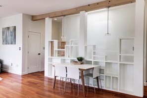 Un'area pranzo moderna con un tavolo e sedie bianchi, travi in legno a soffitto e una mensola bianca con una pianta sopra.
