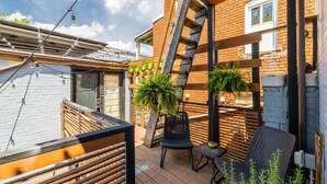 Una terraza de madera con mobiliario exterior, un muro de ladrillo y una escalera de metal.