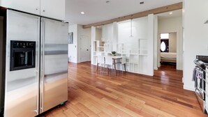 Una cocina moderna con refrigerador de acero inoxidable, piso de madera y armarios blancos.