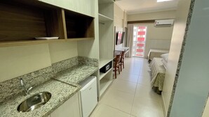 A compact kitchen with a granite countertop, a built-in sink, and a small refrigerator. There is a dining area with a table and chairs, and a bed with a patterned bedspread. - Spazzio diRoma Acqua Park Splash e Slide (Caldas Novas)