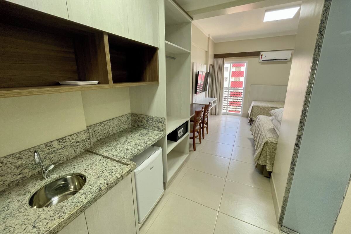 A compact kitchen with a granite countertop, a built-in sink, and a small refrigerator. There is a dining area with a table and chairs, and a bed with a patterned bedspread.
