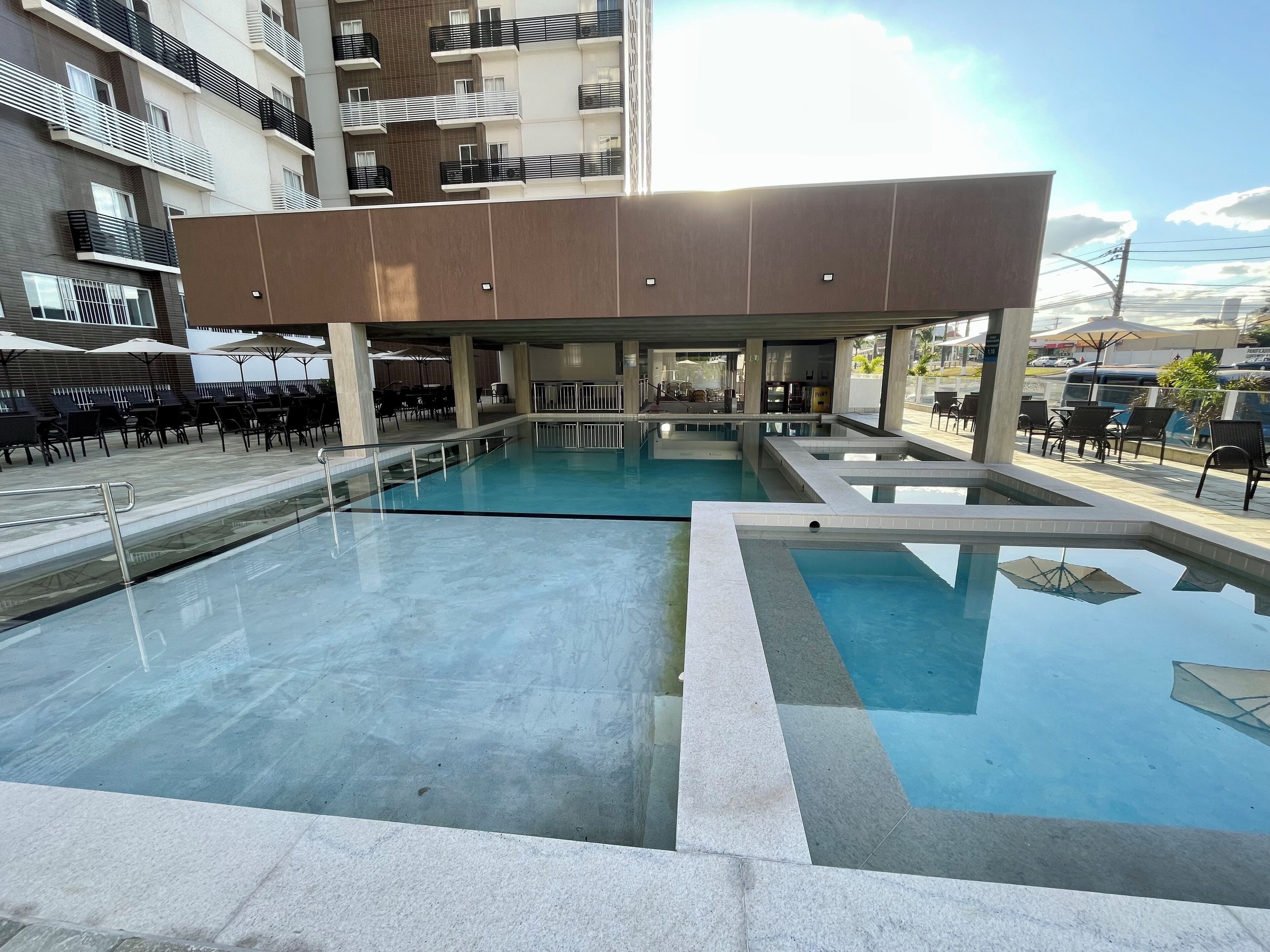 Un área de piscina con varias piscinas, mobiliario exterior y un edificio con balcones.