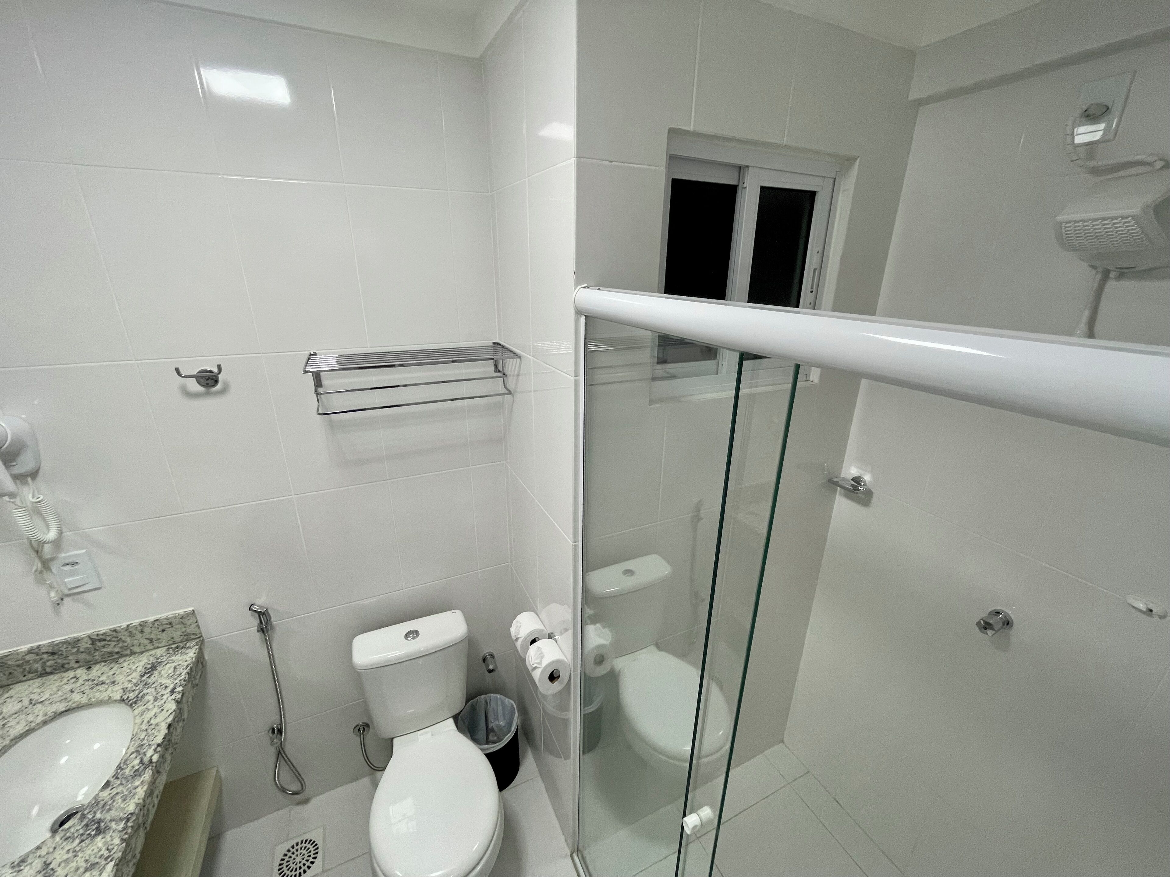 A bathroom with a marble sink, a toilet, a glass-enclosed shower, and a towel rack.
