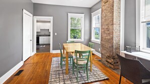 Un comedor con mesa y sillas de madera, pared de acento de ladrillo y vista a la cocina por una puerta abierta.