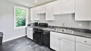 Cocina moderna con armarios blancos, encimera de granito, estufa, horno, lavavajillas y ventana con vistas a zonas verdes.