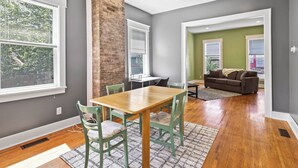 Una sala moderna con comedor, pared decorativa de ladrillo y ventanas grandes.