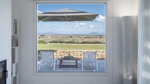 A room with a large window overlooking a scenic landscape, a table with chairs, and a ceiling fan. - Leucosia - Favignana (Favignana)