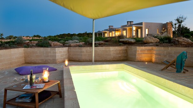 A modern outdoor pool area with a wooden table, a lantern, and a large umbrella.