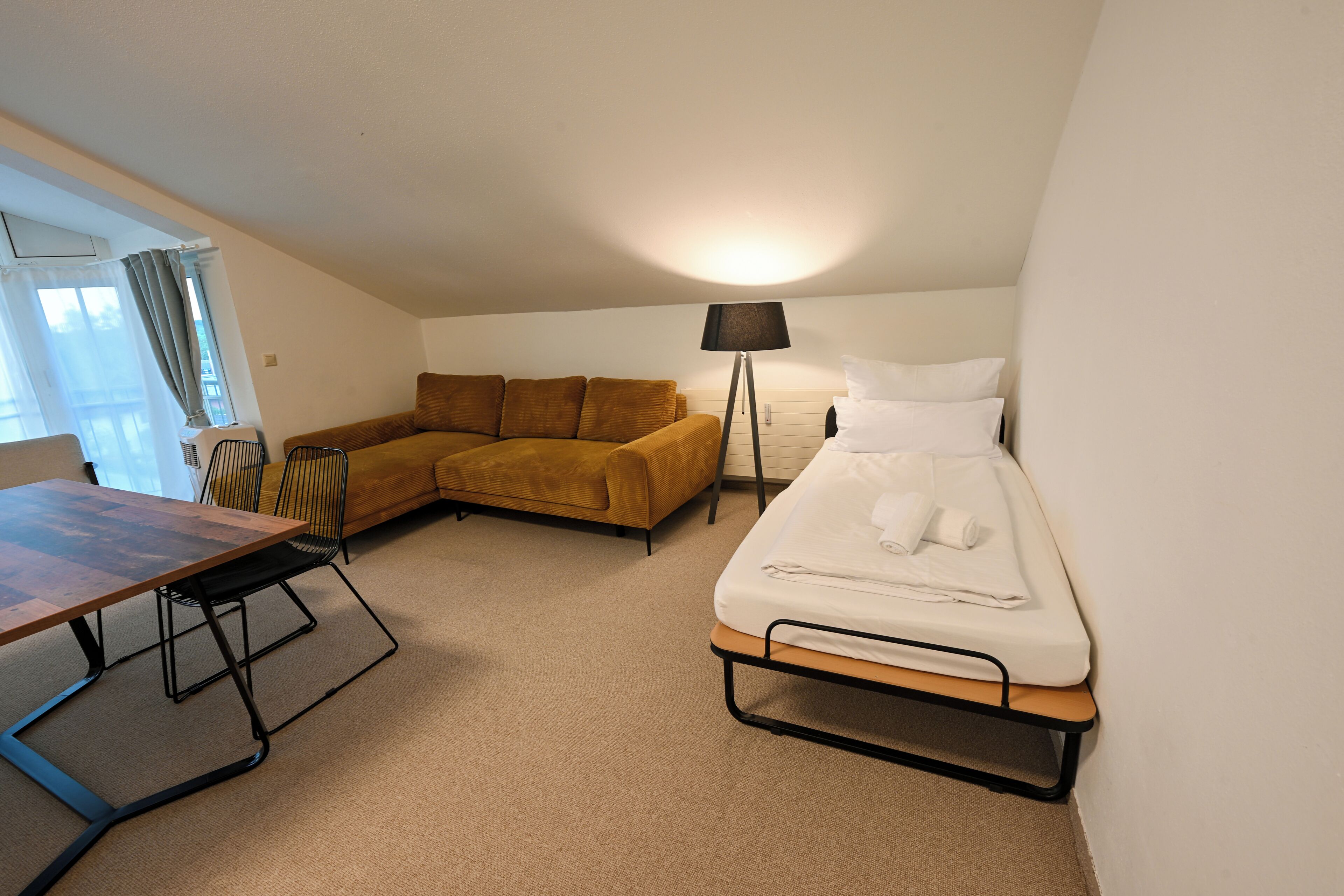 Un petit logement composé d’une seule pièce, comprenant un lit, un canapé, une table et une lampe.