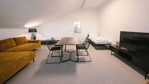 A modern living room with a sofa, a dining table, chairs, a TV, and a window. - ღSunset I Lakeview Ammersee I BBQ I Liboria I 5min from the lake (Herrsching am Ammersee)