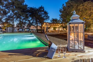 Una terraza de madera con piscina, una botella de champán y una copa de champán.