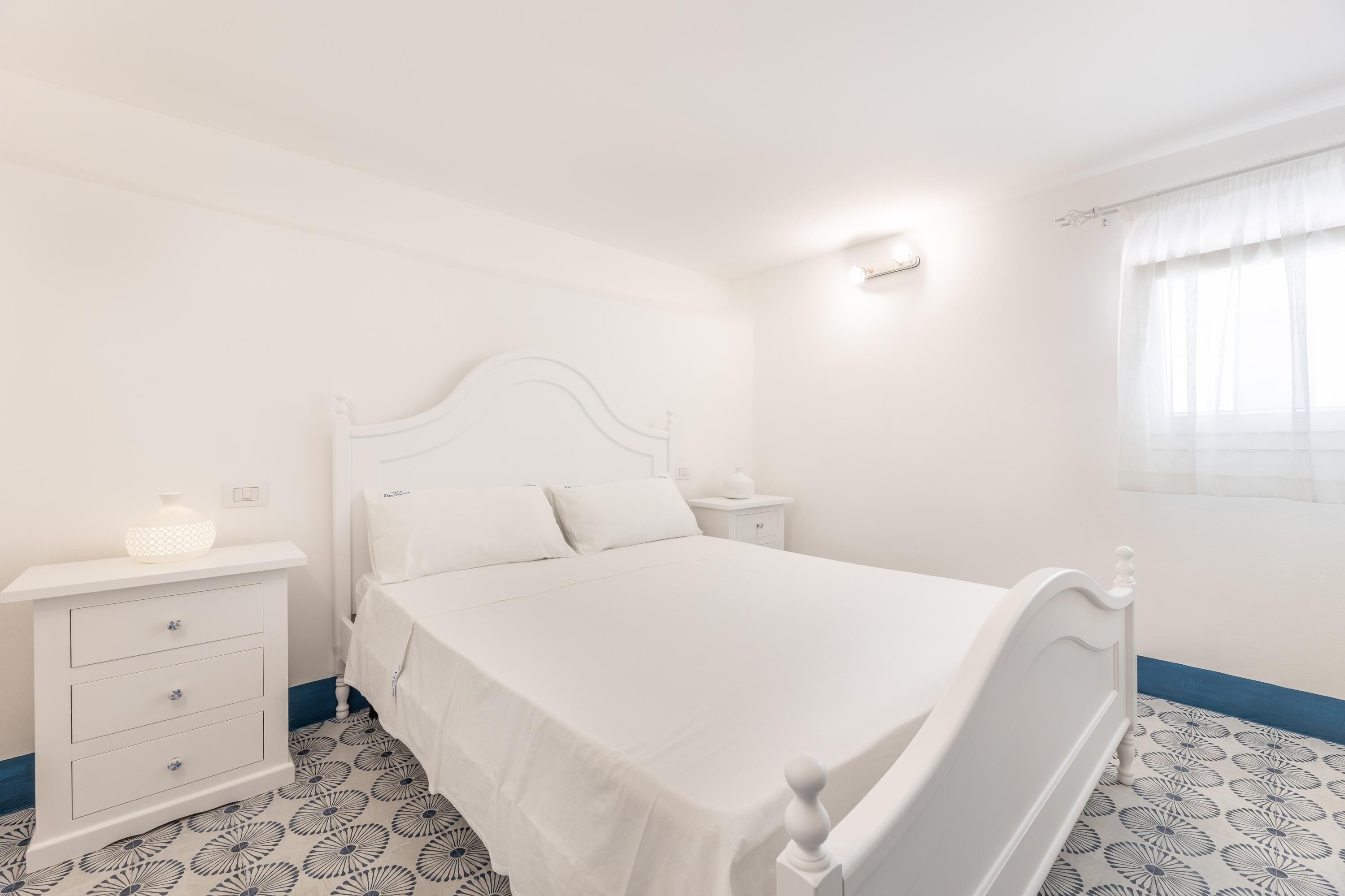 A white bedroom with a bed, a nightstand, and a dresser.