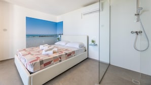 Une chambre d’hôtel moderne avec un lit, une douche en verre et une vue sur la mer.