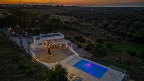Une villa moderne dotée d’une piscine, entourée d’oliviers et offrant une vue panoramique sur le coucher de soleil.