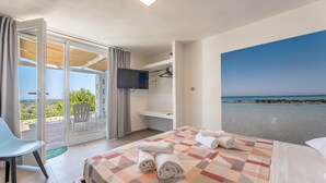 Une chambre d’hôtel avec un lit, une télévision, une chaise et vue sur la plage.