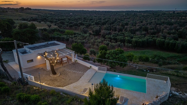 Une villa moderne dotée d’une piscine, entourée d’un jardin aménagé et offrant une vue sur la campagne au coucher du soleil.