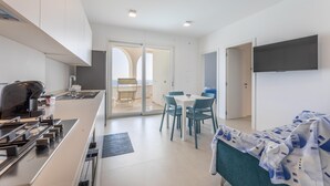 Een moderne keuken met een gasfornuis, een koffieapparaat en een eethoek met een tafel en stoelen.