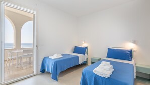 Een kamer met twee bedden, elk met een blauw sprei en kussens, en een tafel met stoelen.