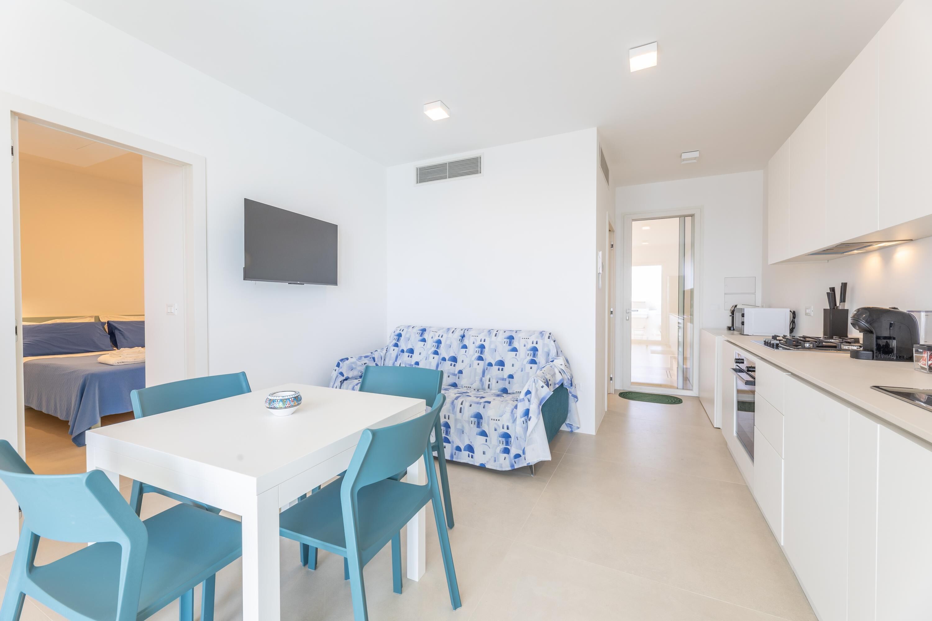 A modern, compact living space with a dining area, kitchenette, and a sofa with a patterned cover.