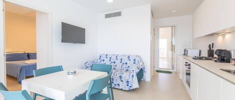 A modern, compact living space with a dining area, kitchenette, and a sofa with a patterned cover.