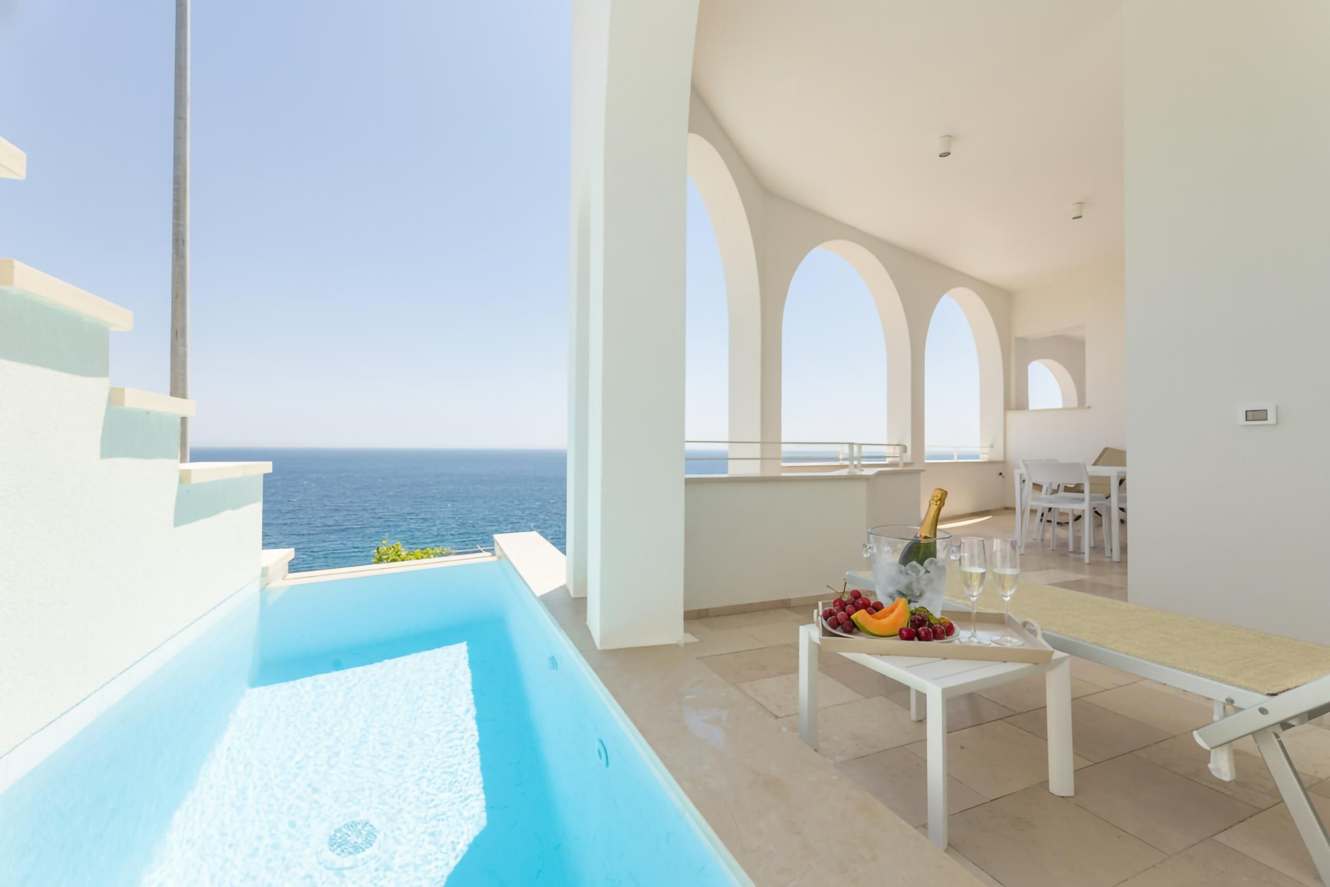 Un interior moderno con piscina, un comedor con mesa para dos y vista al mar.