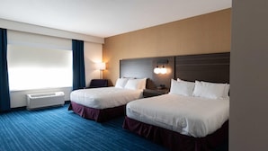 Habitación de hotel con dos camas, un escritorio, una silla, una lámpara y una ventana con cortinas.