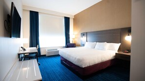 Habitación de hotel con cama, mesitas de noche, escritorio con silla, televisor y ventana con cortinas.