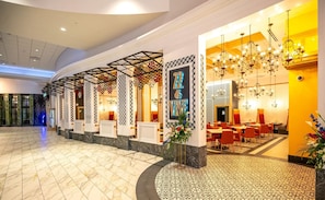 A hotel lobby with a marble floor, a reception area with a '22 & VINE' sign, and a dining area with tables and chairs.