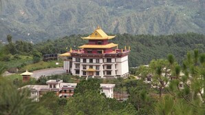 A traditional multi-story building with a distinctive yellow roof, surrounded by lush greenery and hills. - Neydo Hotel Buddhist Monastery (Dakshinkali)