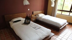 A hotel room with two beds, a wooden headboard, a nightstand with a lamp, and a window with curtains. - Neydo Hotel Buddhist Monastery (Dakshinkali)