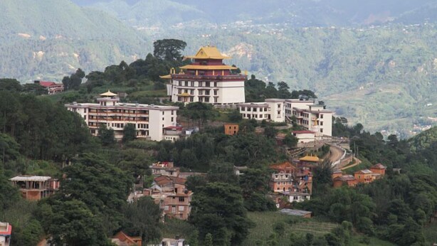 A traditional building with a yellow roof, surrounded by lush green hills and other residential buildings. - Neydo Hotel Buddhist Monastery (Dakshinkali)