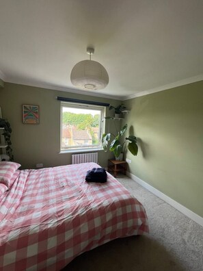 Cozy bedroom with a checkered bedspread, radiator, and potted plant.