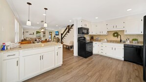 Una cocina amplia con armarios blancos, un refrigerador negro y piso de madera.