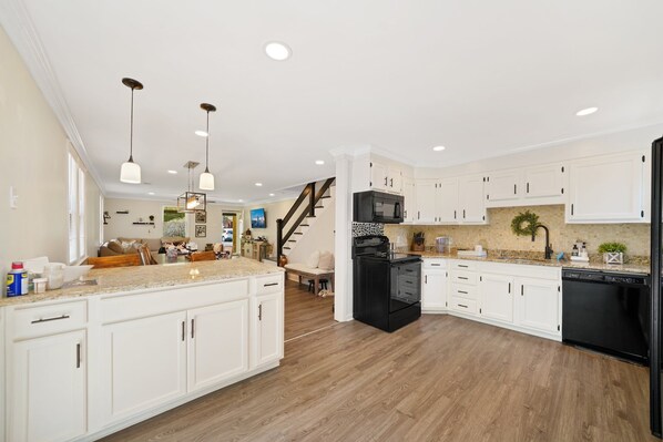 A spacious kitchen with white cabinetry, a black refrigerator, and a wooden floor.