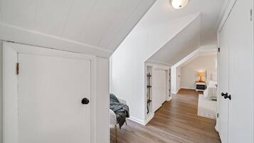 Un corridoio con pareti bianche e pavimento in legno, che conduce a una camera da letto con un letto e un comodino.