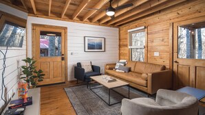 A cozy cabin interior with a wooden ceiling, a sofa, a coffee table, and a television on a stand.