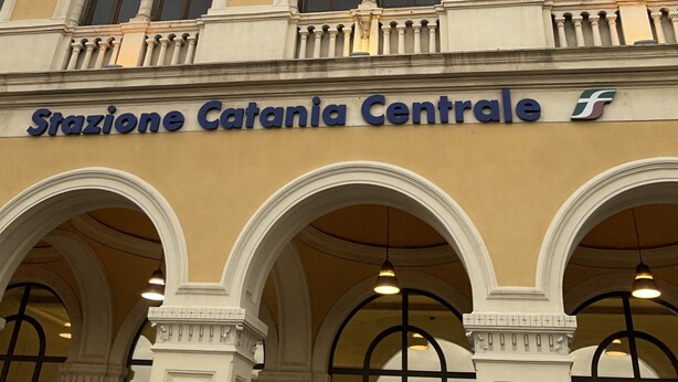 Un edificio con il cartello "Stazione Catania Centrale". Presenta uno stile architettonico classico, caratterizzato da finestre ad arco e colonne.