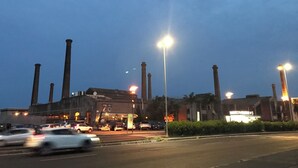 Un grande edificio industriale con numerose ciminiere, un parcheggio con auto e lampioni.