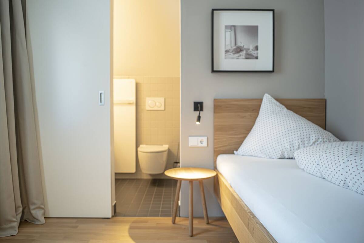 A hotel room with a bed, a bedside table, a wall-mounted picture, and a view into the bathroom.