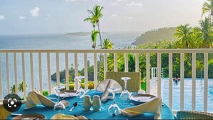A balcony with a table set for dining, overlooking a pool and a coastal view. - Wake Up At Paradise (Santa Barbara Samana)