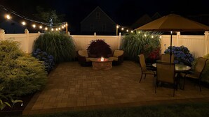 Une terrasse avec un foyer, des meubles d’extérieur, des guirlandes lumineuses et un parasol.