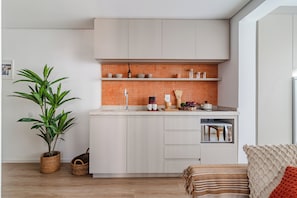 Een moderne keuken met witte kastjes, een achterwand van baksteen en een potplant.