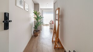 Un pasillo con una planta en maceta, cuadros enmarcados, un caballete de madera y un sofá blanco al fondo.