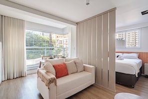 Een moderne hotelkamer met een groot raam, een bank, een bed en een nachtkastje.