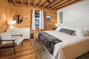 A wooden cabin bedroom with a bed, a chair, a desk, and a mirror. - Red Feather Cabins 282 (Boone)
